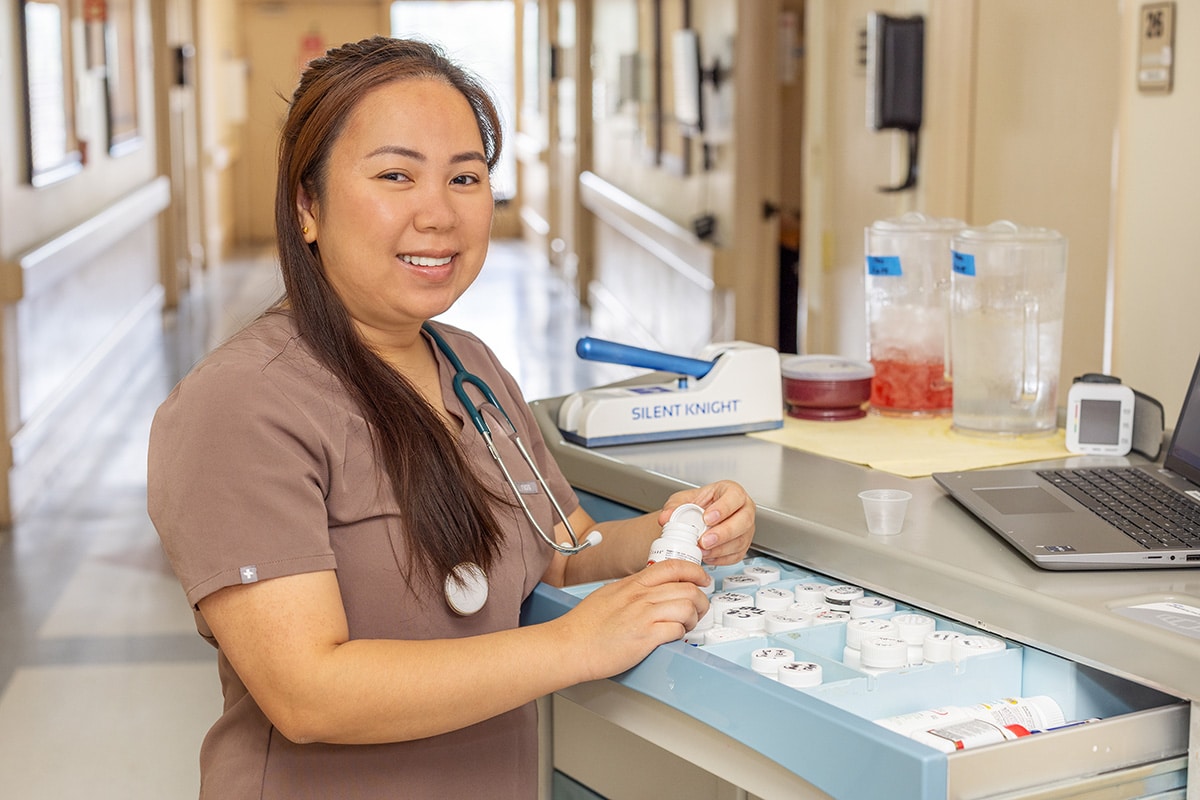A caregiver standing at a nurse's cart in the hallway at the Sunrise Post Acute facility