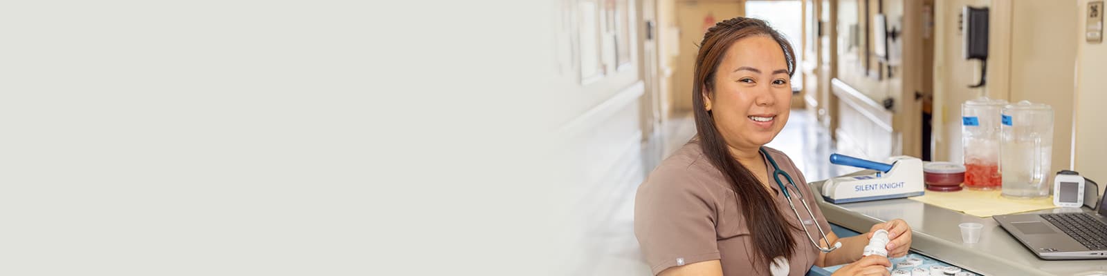 A caregiver standing at a nurse's cart in the hallway at the Sunrise Post Acute facility